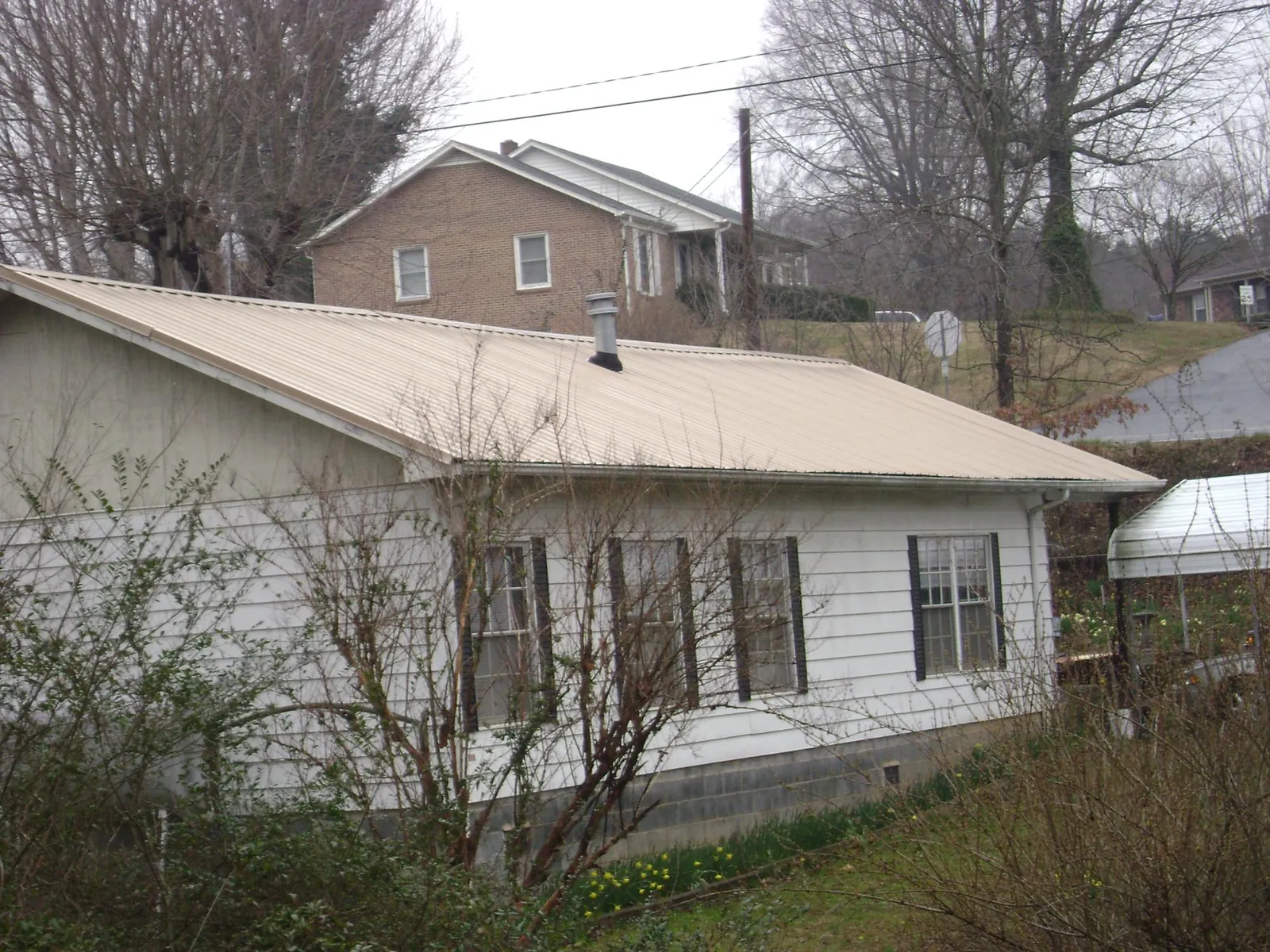 Tan metal roof on a white sided house set into a hillside — Commercial Roofing by Roofing Brothers in Lincoln